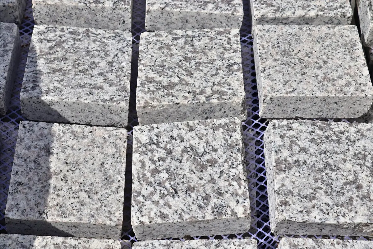 Pavés de granit gris clair taillés en cubes, vus de près, surface clivée mouchetée